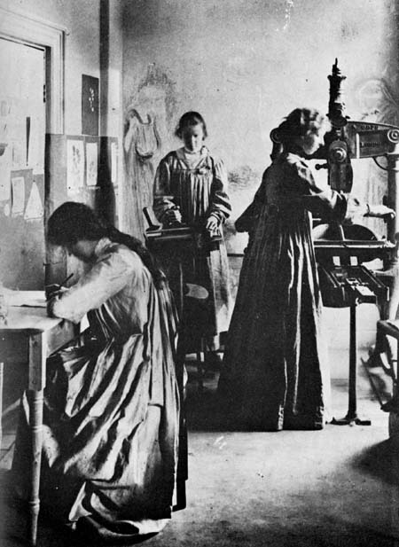 Three women in long cloaks writing and working with an old print press.